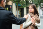 Homem seguindo mulher na rua e encostando em seu ombro. A mulher olha com para o homem incomodada, e estende sua mão para ele se distanciar.