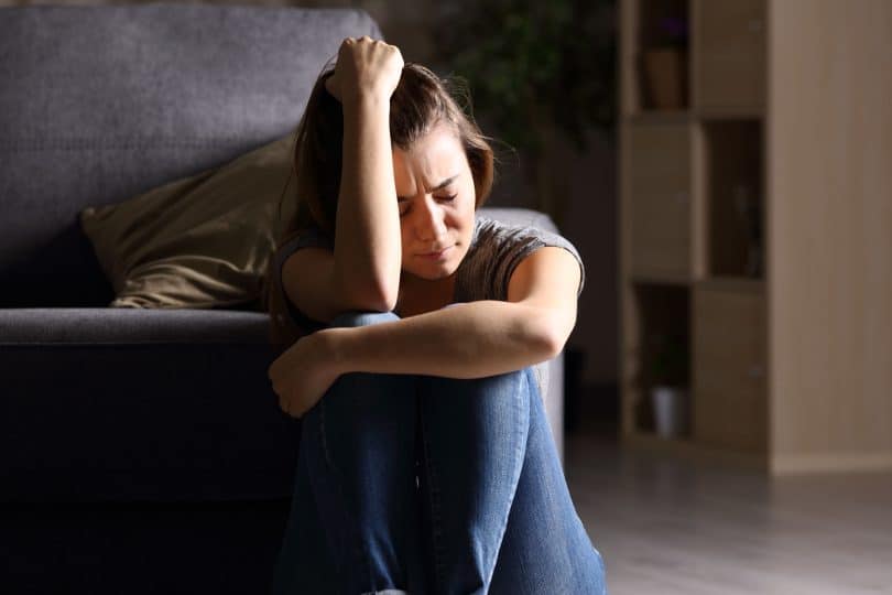 Vista frontal de uma adolescente triste sentado no chão na sala de estar em casa com um fundo escuro