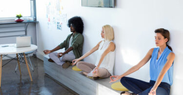 Três pessoas meditando em escritório.