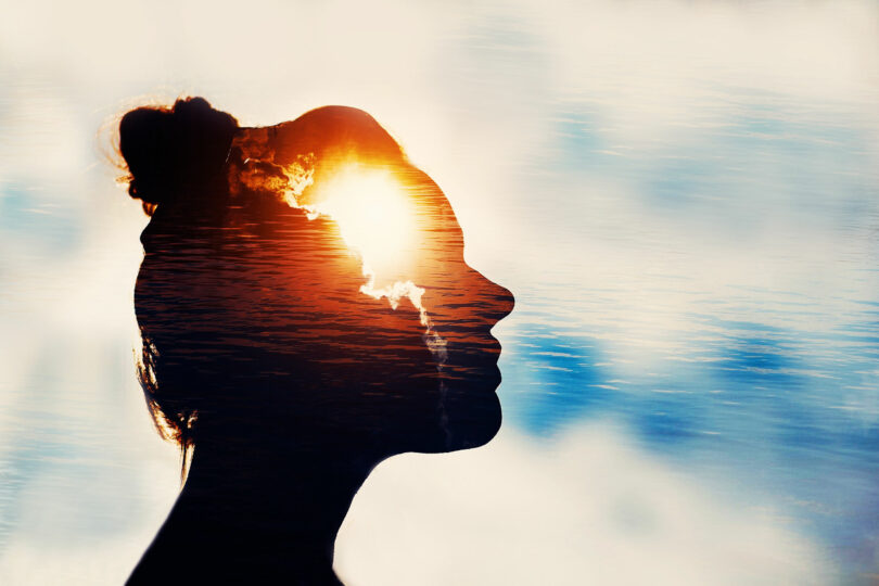 Silhueta de rosto feminino com imagem de luz dentro e céu com nuvens ao fundo