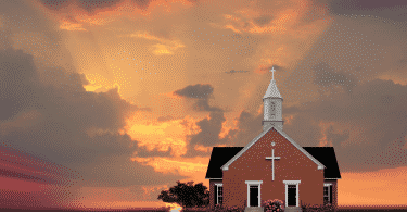 Imagem de uma igreja no meio do campo, ao entardecer.