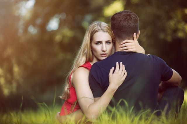 Casal sentado na grama com homem de costas e mulher de frente para foto