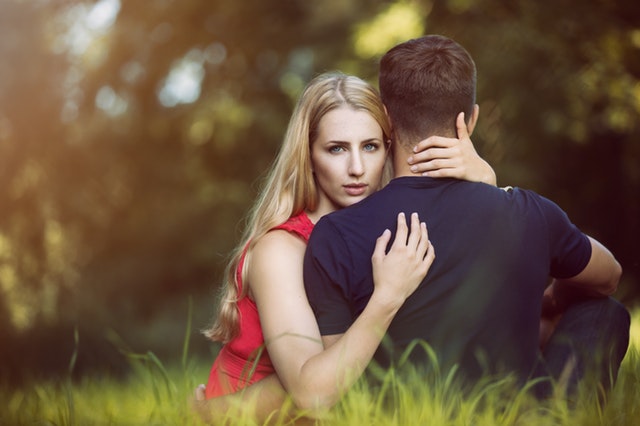Casal sentado na grama com homem de costas e mulher de frente para foto