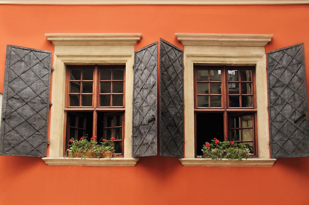 Parede externa de um quarto pintada na cor laranja. Temos duas janelas grandes de madeira e cada uma delas possui um floreira.
