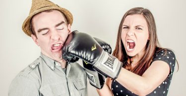 Casal de homem e mulher simulando uma briga. Ela usa uma luva de boxe e está simulando um soco no rosto do homem.