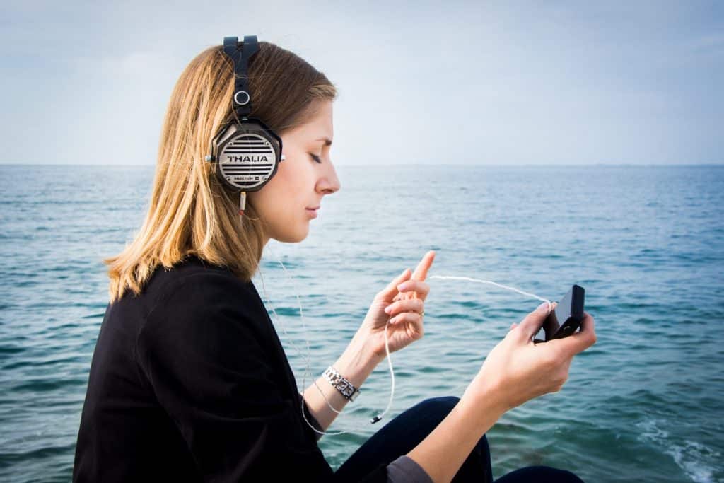 Mulher sentada ao lado de um mar ouvindo música no fone de ouvido