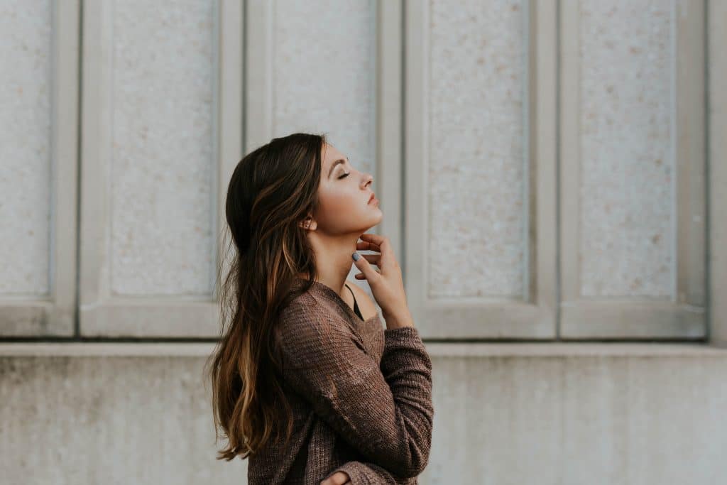 Mulher de perfil com olhos fechados e mão no pescoço