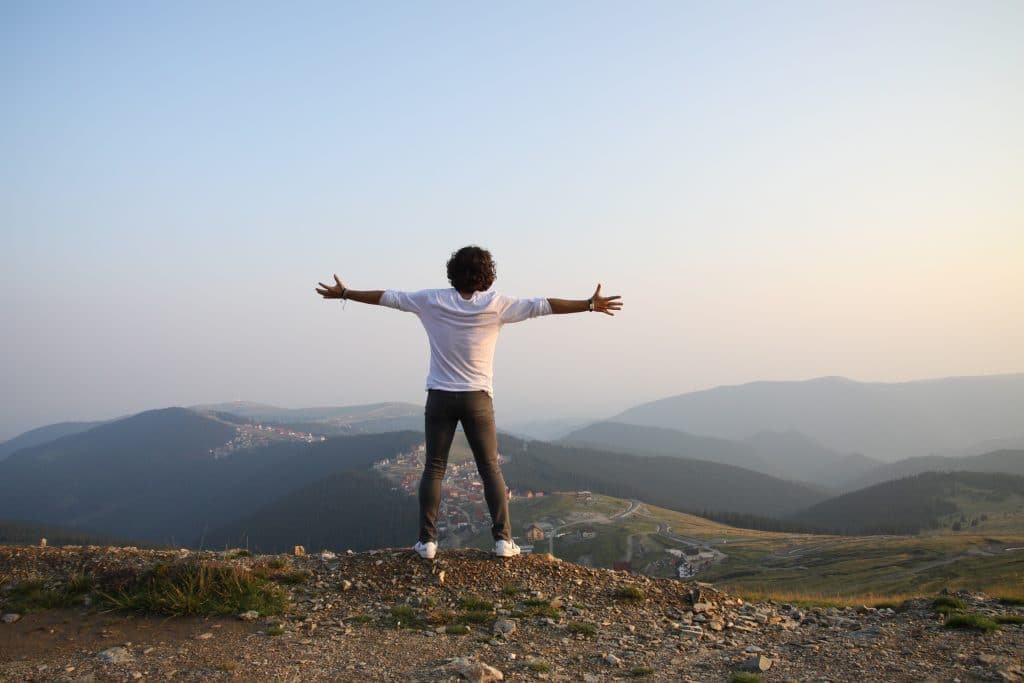 Homem com os braços abertos olhando para o horizonte com montanhas