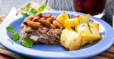 Prato azul com um pedaço de bolo de carne com nozes e batata assada.