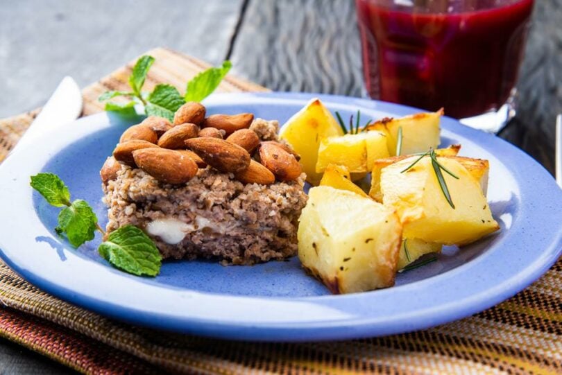 Prato azul com um pedaço de bolo de carne com nozes e batata assada.