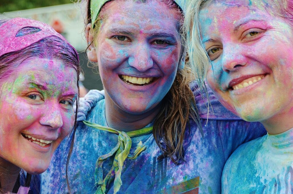 Três garotas sorrindo. Todas estão com o rosto pintado e colorido. 