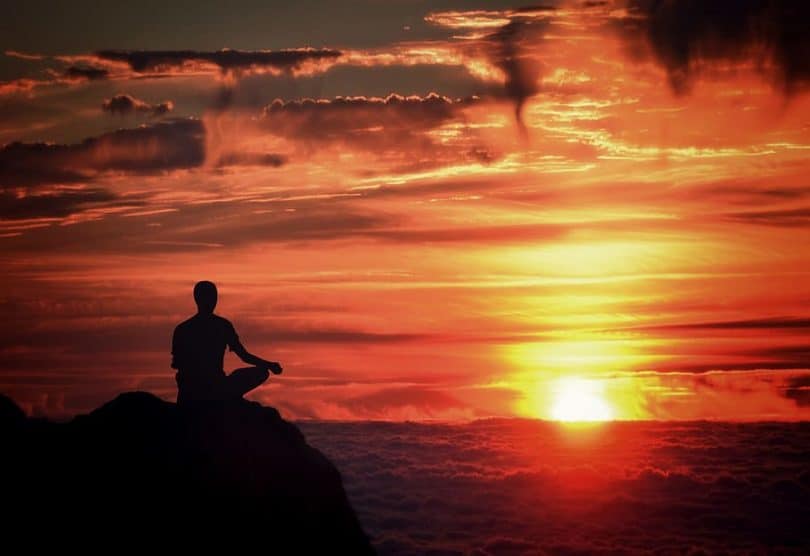 Pessoa sentada com as pernas cruzadas em uma montanha durante o nascer do sol.