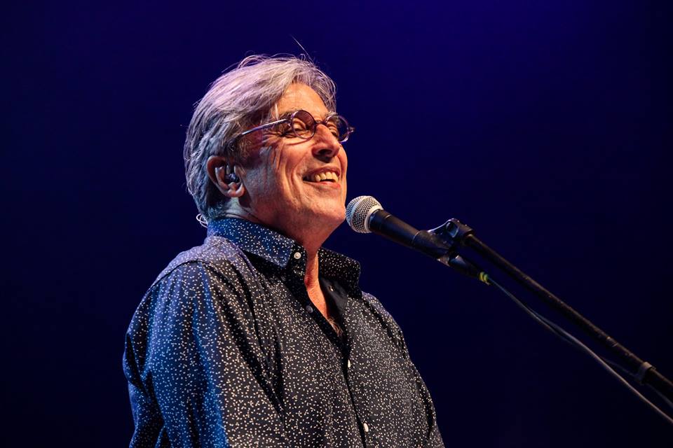 Fotografia de Ivan Lins cantando em um microfone enquanto sorri.