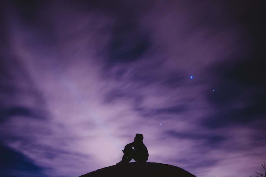 Silhueta de um homem sentado observando o céu à noite.