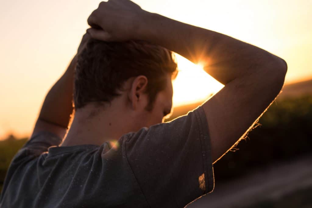 Homem de costas com mão na cabeça e sol refletindo ao fundo