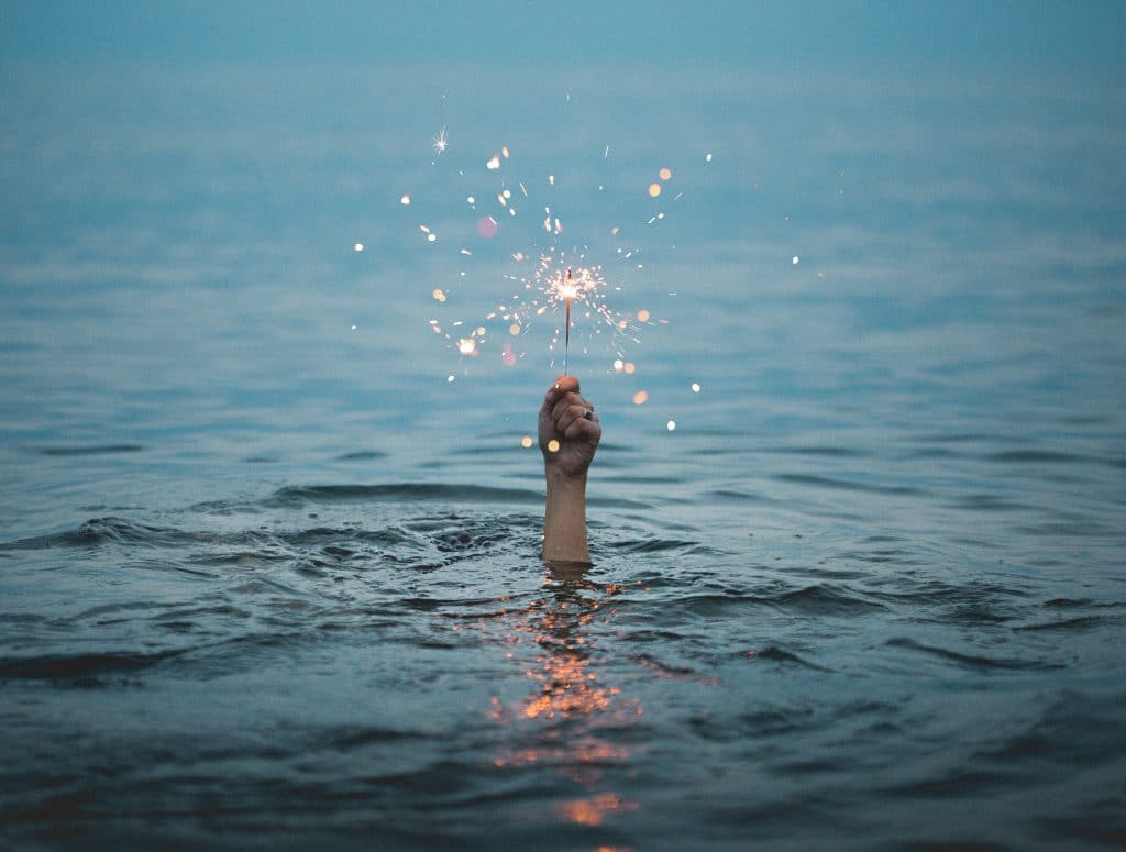 Mão segurando uma vela acesa emerge da água.