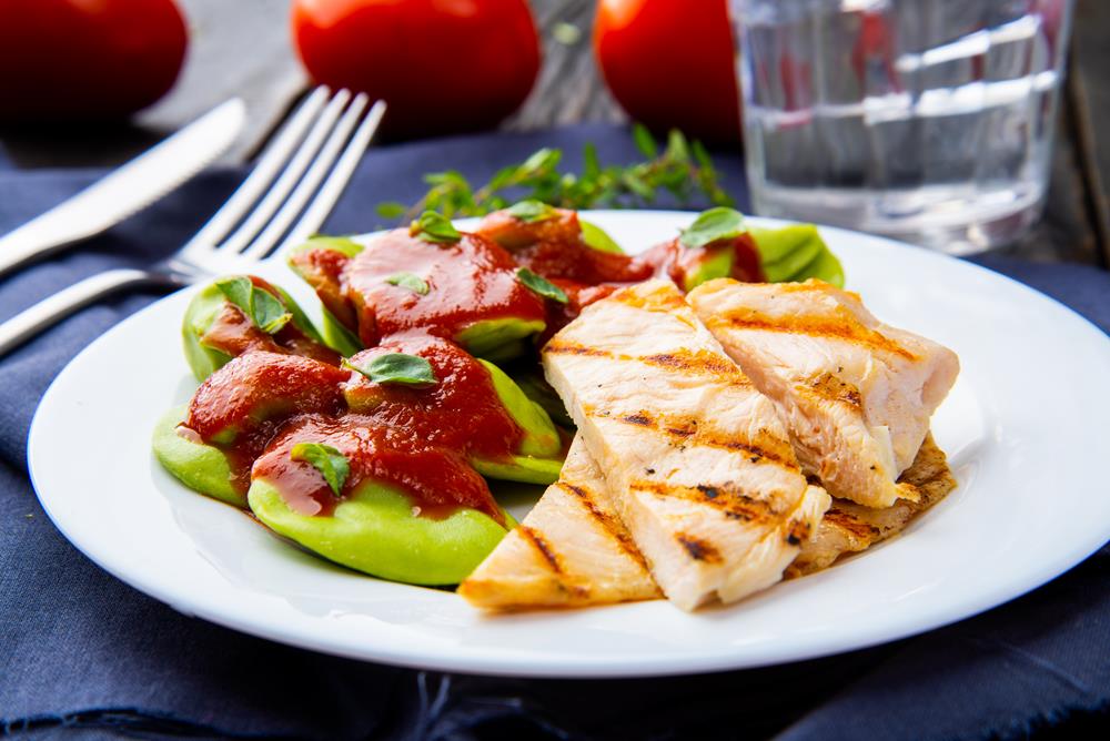 Prato branco com uma massa verde acompanhada de pedaços de frango.