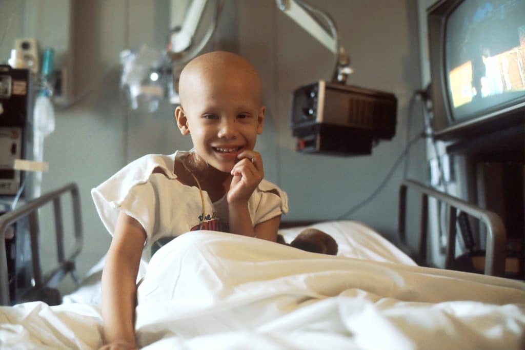 Criança vítima de câncer em uma maca de hospital, sorrindo.