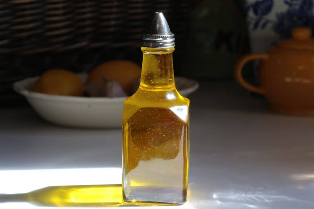 Frasco de óleo usado para culinária em uma mesa, à frente de uma bacia com frutas.
