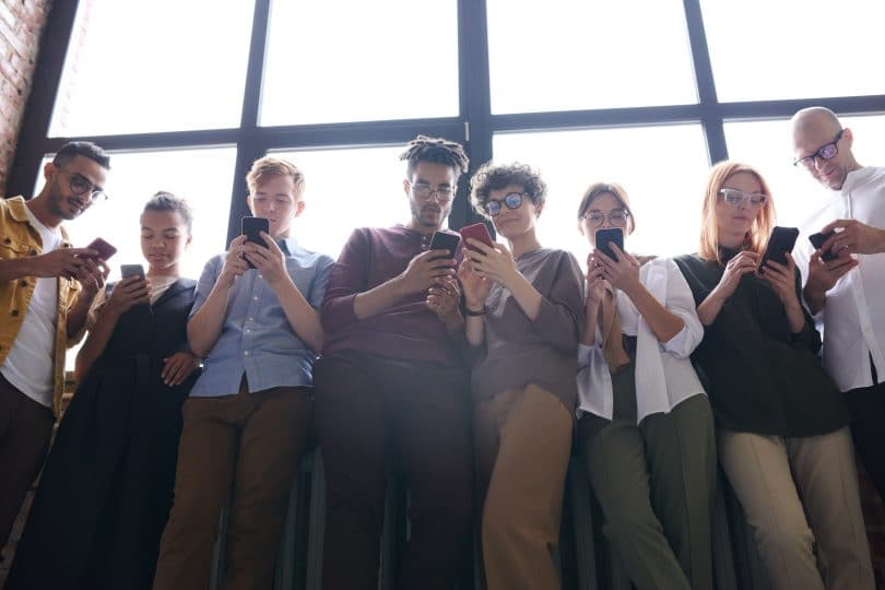 Pessoas encostadas em parede respondendo mensagens em seus celulares