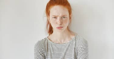 Mulher fazendo careta de teimosia. Ela veste uma blusa listrada e está sobre um fundo branco.