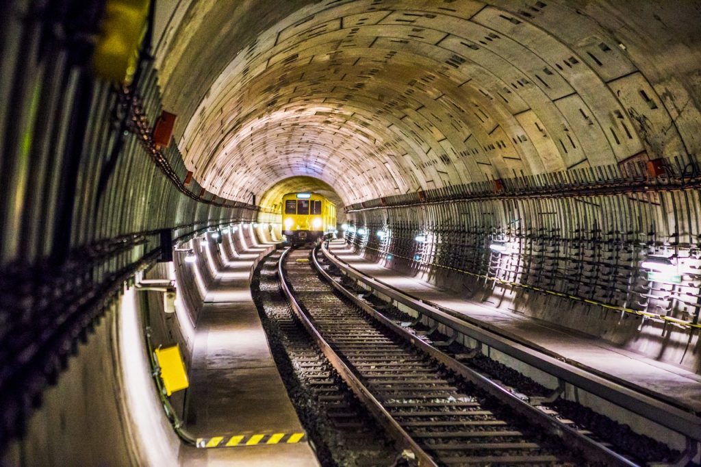 Trem amarelo passando por um túnel., em direção à câmera.