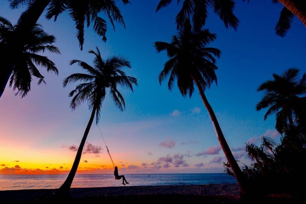 Menina sentada no balanço na praia admirando o entardecer. 