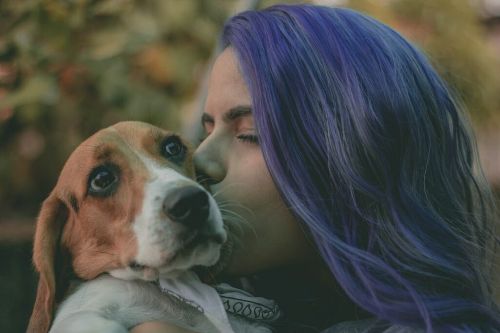 Mulher segurando cachorro branco e marrom em seu colo, enquanto lhe da um beijo na cabeça.