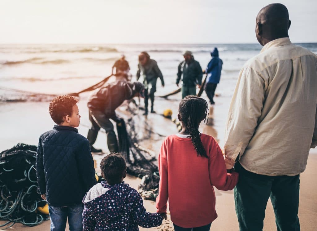 Crianças refugiadas param em frente ao mar, com um adulto e uma equipe de busca.