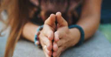 Recorte das mãos de uma mulher ajoelhada com as mãos em forma de prece representando a gratidão.