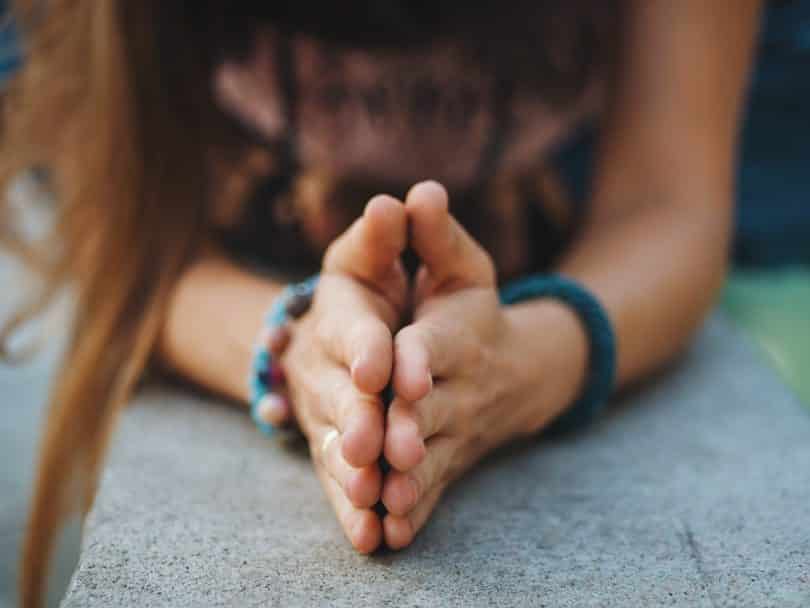 Recorte das mãos de uma mulher ajoelhada com as mãos em forma de prece representando a gratidão.