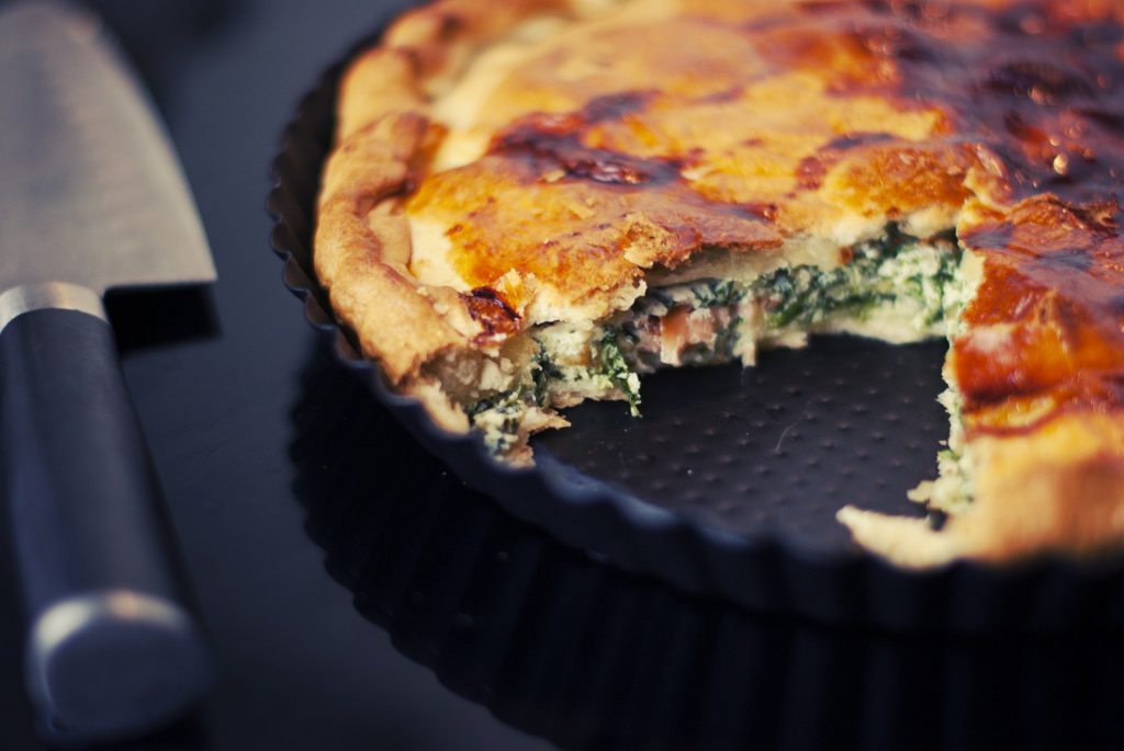 Quiche de espinafre assada. Ela está em uma forma redonda de TFAL e ao lado uma faca para poder cortar.