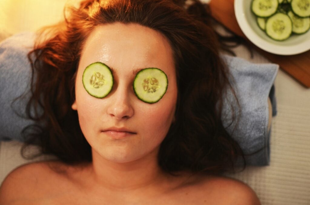 Mulher deitada com a cabeça sobre uma toalha e rodelas de pepinos nos olhos.