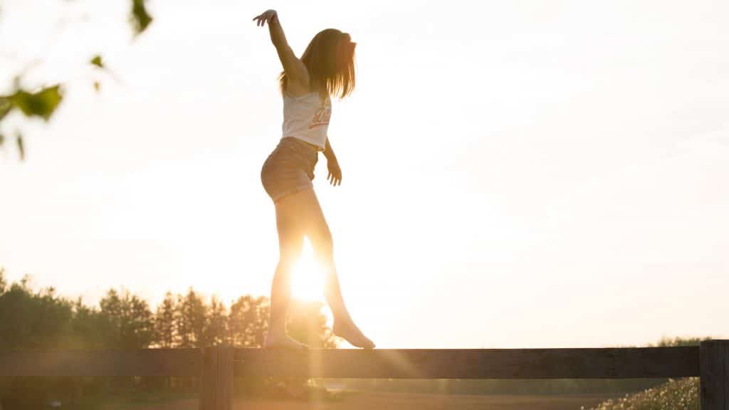 Mulher equilibrando-se em ponte de madeira com sol refletindo ao fundo