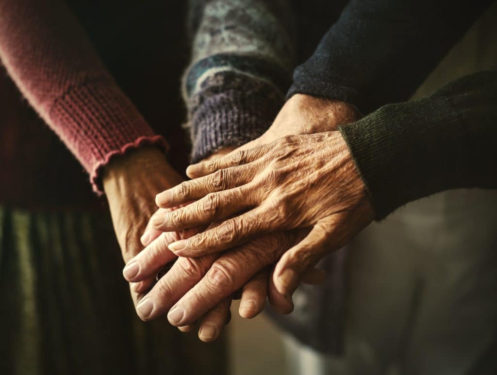 Imagem de várias mãos de pessoas idosas, umas sobre as outras. Trazendo um sentimento de compaixão e simpatia.