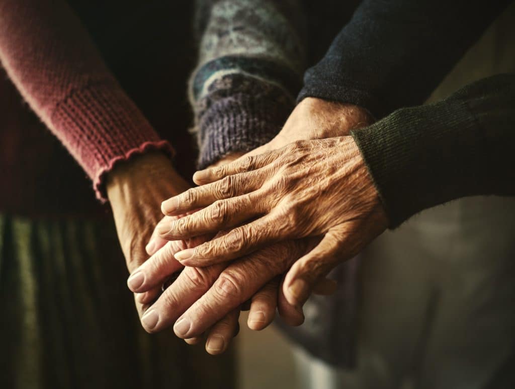 Imagem de várias mãos de pessoas idosas, umas sobre as outras. Trazendo um sentimento de compaixão e simpatia.
