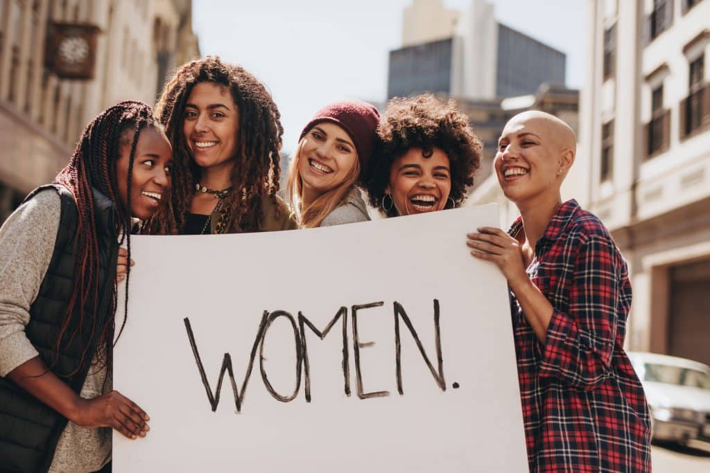 Mulheres em um protesto de empoderamento feminino segurando cartaz escrito em inglês "mulheres"