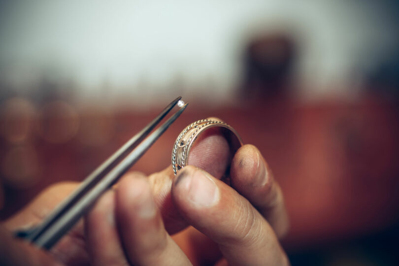 Ourives colocando um diamante em um anel com uma pinça.