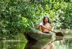 Homem indígena andando de canoa em rio.