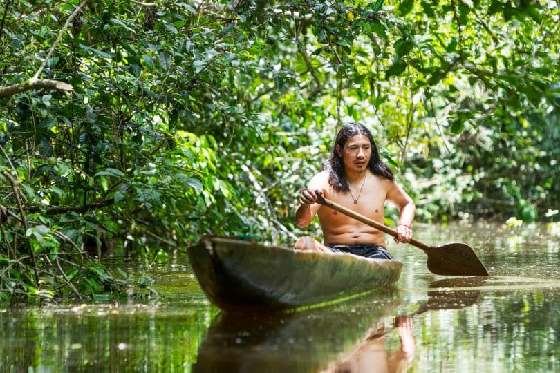 Homem indígena andando de canoa em rio.