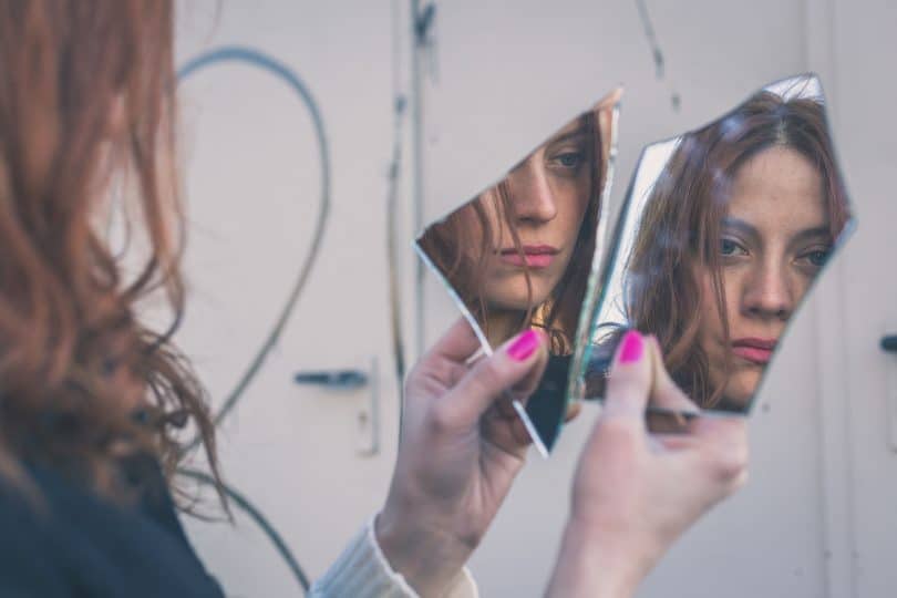 Mulher olhando seu reflexo no espelho triste