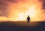 Silhueta de um homem em pé, de costas, em um campo sob o pôr do sol.