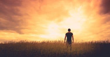 Silhueta de um homem em pé, de costas, em um campo sob o pôr do sol.