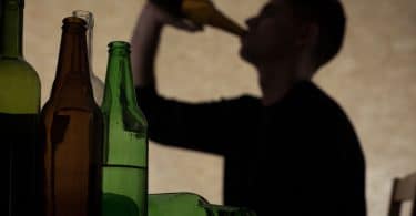 Sombra de jovem bebendo com garrafas de bebida vazias em foco