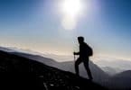 Silhueta de pessoa caminhando em direção ao topo de uma montanha, usando capuz e mochila.