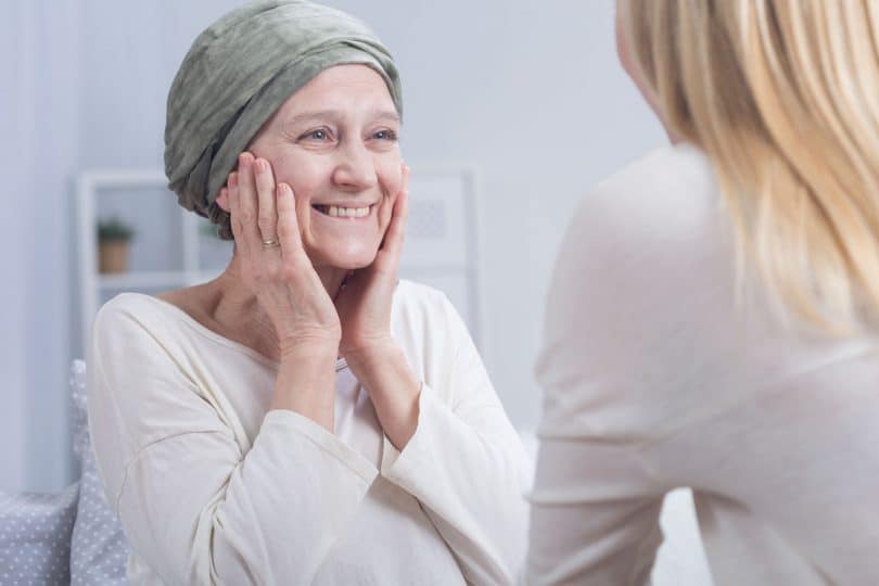 Mulher com câncer olhando e sorrindo para outra mulher a sua frente