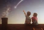 Menino e menina sentados no telhado de casa de costas olhando para estrela cadente