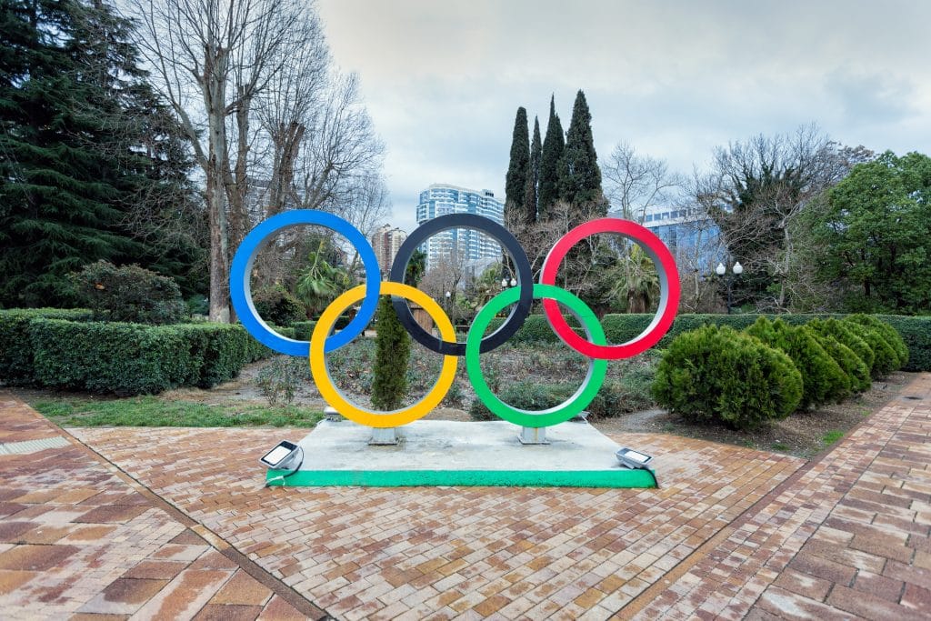 Imagem dos anéis do símbolo das Olímpiadas feito em formato de uma estátua. Ele está disponível em um lindo jardim.
