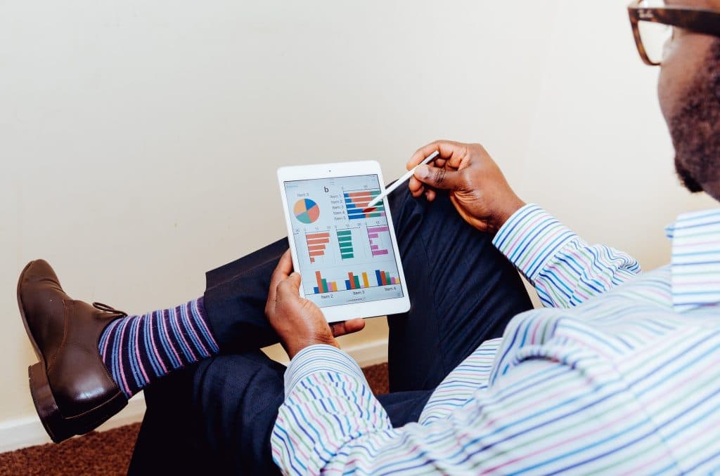 Homem sentado com iPad na mão analisando gráficos