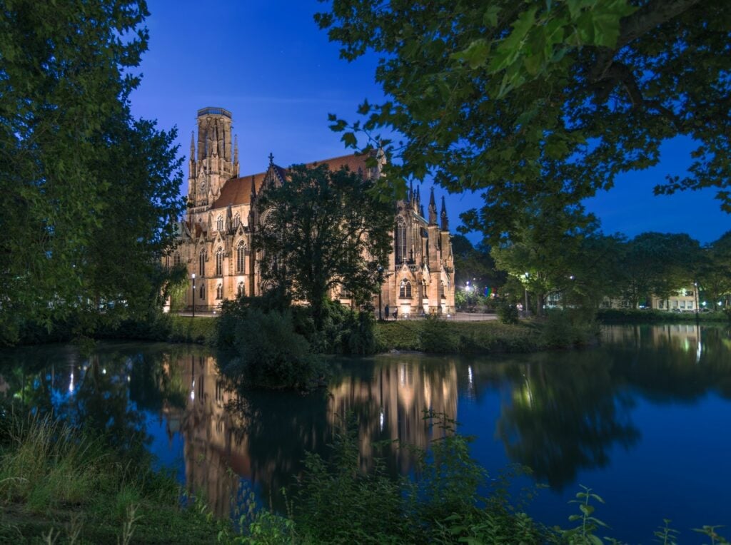 Castelo antigo, cercado por árvores e um lago, durante a noite.